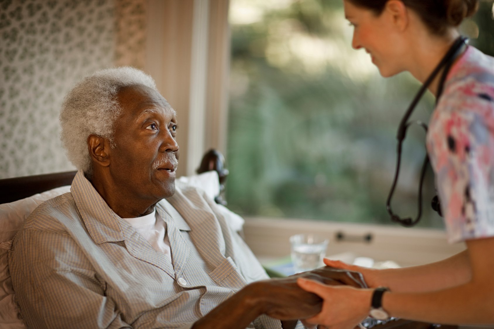 A smiling nurse holds the hand of a senior resident in a long term care homeA nurse holds the hand of a smiling senior resident in a long term care homeabout-jubo-hero-caregiver-resident