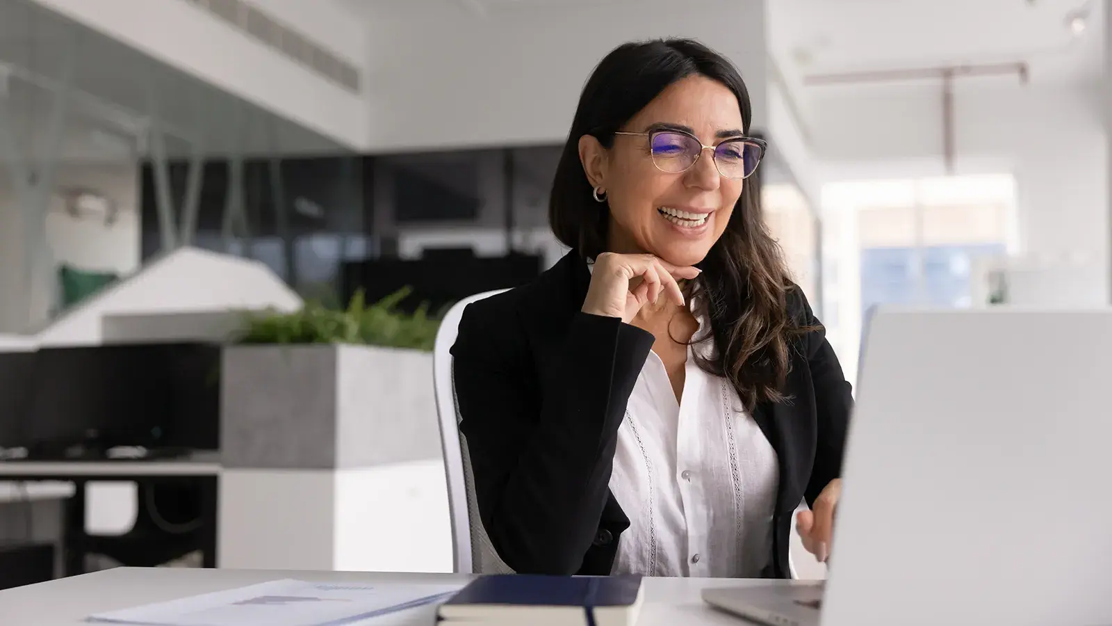 Smiling senior care leader in glasses reading on her laptop at an office desk